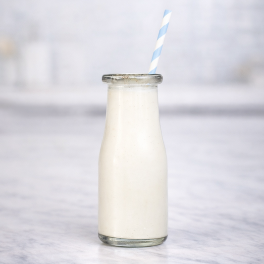 Glass bottle of milk with a straw on a marble surface