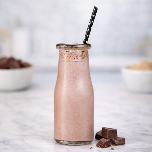 Glass bottle of chocolate milkshake with a straw on a marble surface, surrounded by chocolate pieces.