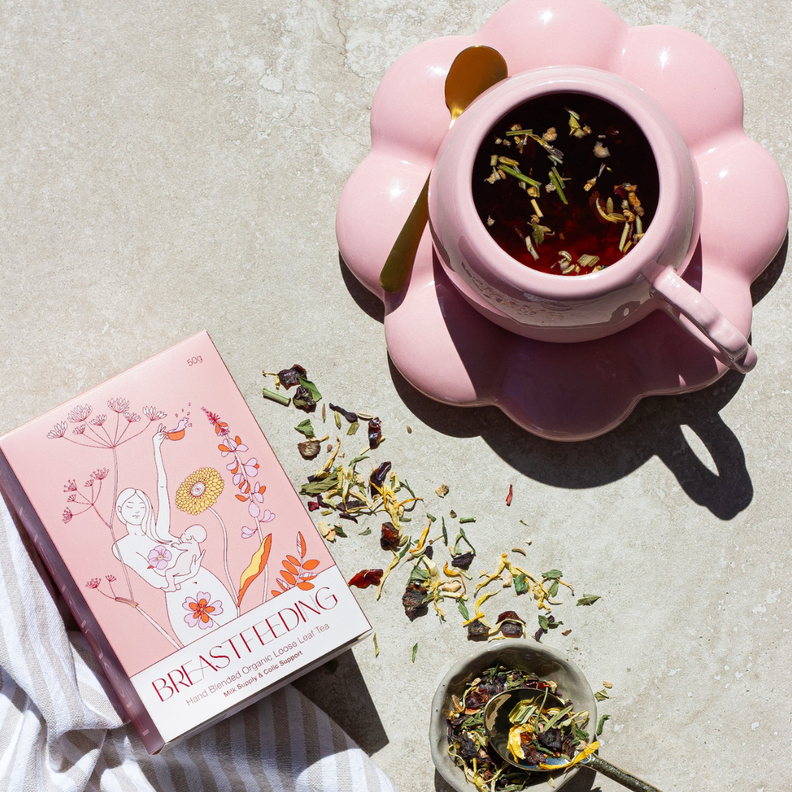 Pink teacup with tea leaves, a box of tea, and a white towel on a light surface.