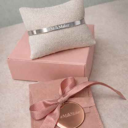Pink packaging with a gold disc and ribbon, featuring 'Milk Maker' branding, on a light gray surface.