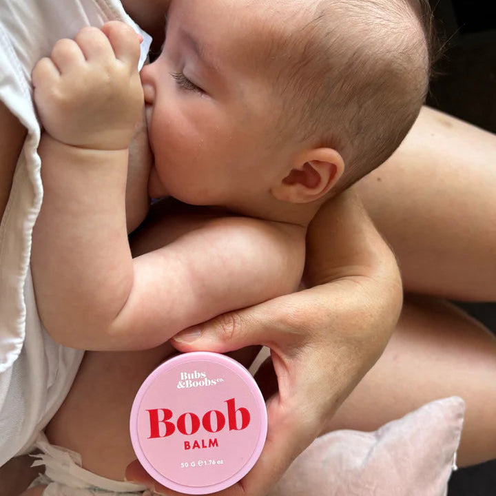 Baby being held by a person with a 'Boob Balm' container visible