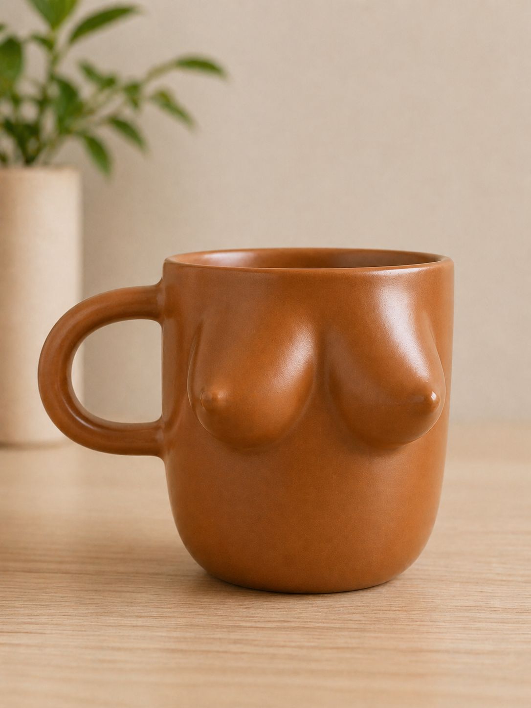 Ceramic mug shaped like a female torso on a wooden surface with a plant in the background.