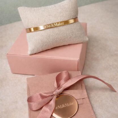 Pink jewelry box with a gold disc and ribbon, and beige pillow with 'Milk Maker' band on a light gray background.