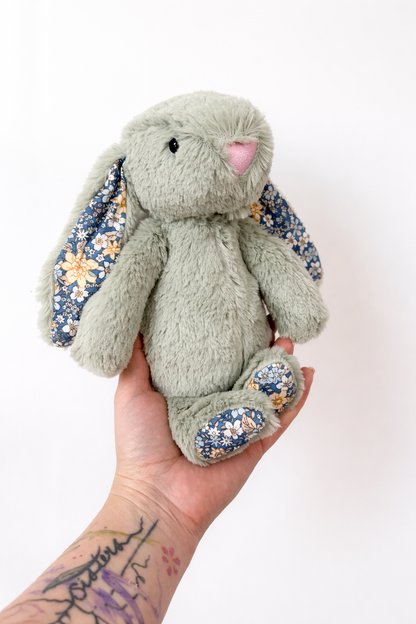Hand holding a soft toy rabbit with floral ears against a white background