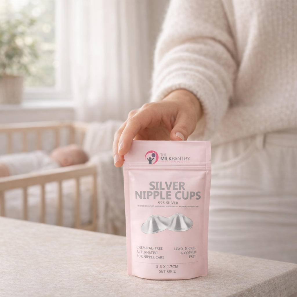 Person holding a pink package of 'Silver Nipple Cups' with a baby crib in the background.