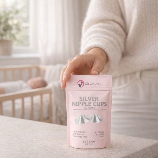 Person holding a pink package of 'Silver Nipple Cups' with a baby crib in the background.