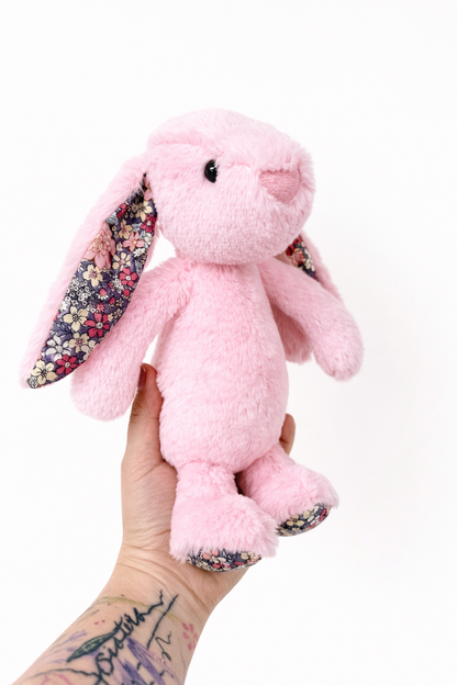 Pink plush bunny with floral ears held by a hand on a white background