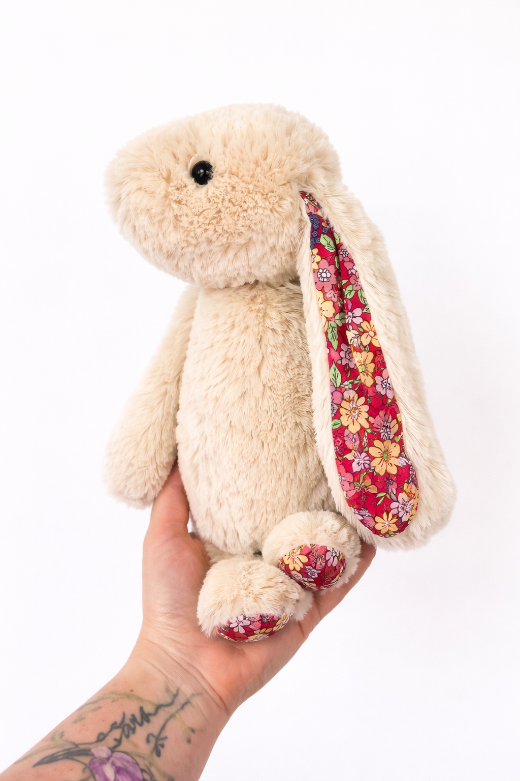 Plush bunny with floral ear held in a hand on a white background