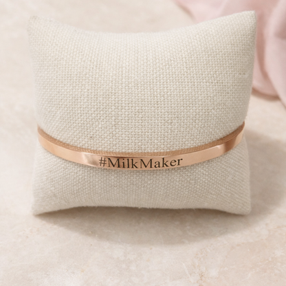 Rose gold bracelet with 'Milk Maker' engraving on a textured beige pillow