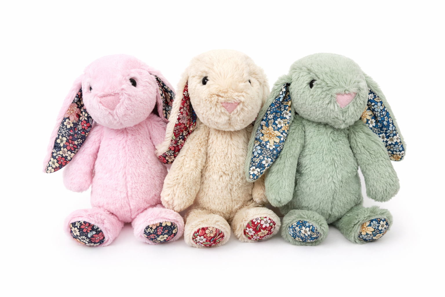 Three plush bunny toys in pink, beige, and green on a white background