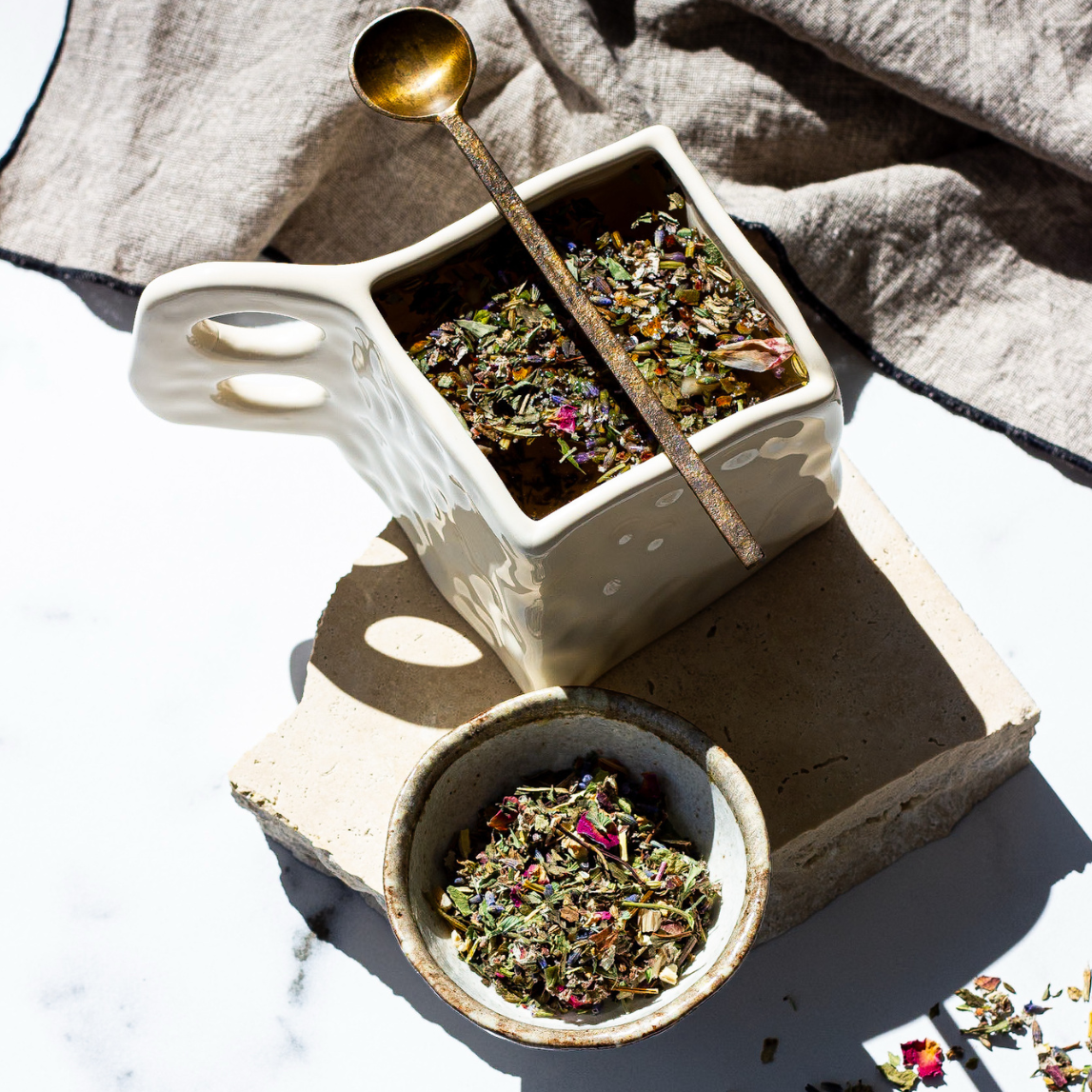 Tea leaves in a small white container with a gold spoon on a marble surface.
