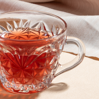 Clear glass teacup with red liquid on a beige fabric background