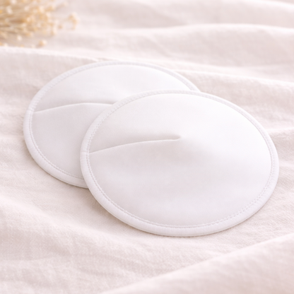 Two white reusable nursing pads on a soft beige fabric background.